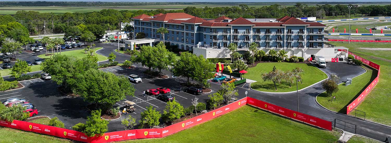 Aerial view of hotel at Sebring International Raceway during Ferrari Challenge event with racetrack, parking lot, and branded red barriers